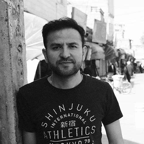 Black and white portrait of Afghani-Australian artist Elyas Alavi. Elyas has short, dark hair and beard and wears a black t-shirt with wite writing on it.jpg