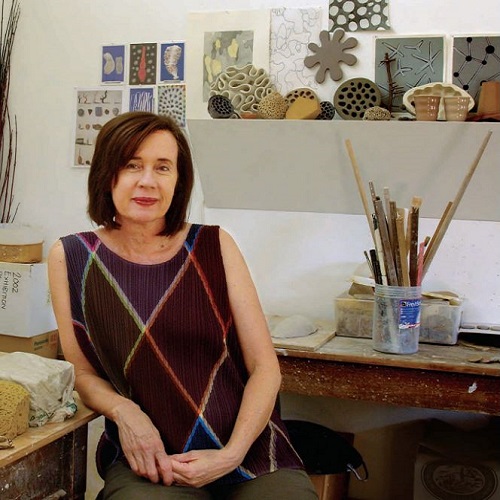 Portrait of Angela Valamanesh sitting in her studio. Angela is a Caucasian female with shoulder length dark brown hair wearing tan pants and a patterned, sleeveless top.JPG