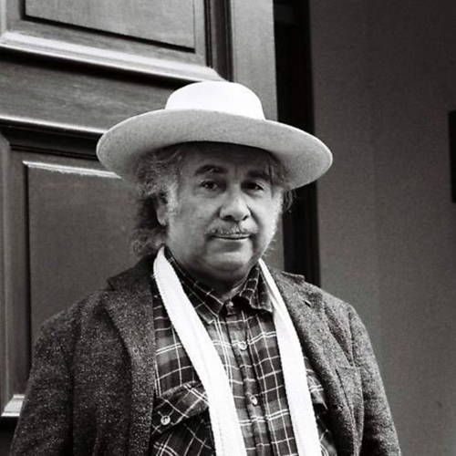Black and white portrait of Aboriginal artist, curator and writer Djon Mundine, wearing a broad brimmed hat, checked shirt, tweed jacket and skinny scarf draped around his neck.jpg