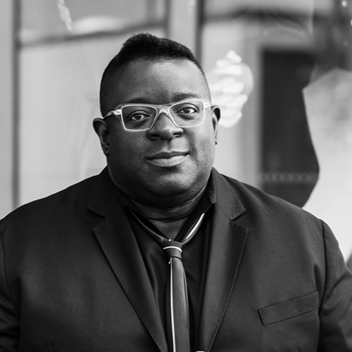 Black and white portrait of Isaac Julien, a black man with short dark hair wearing wire-framed glasses and a dark suit.jpg